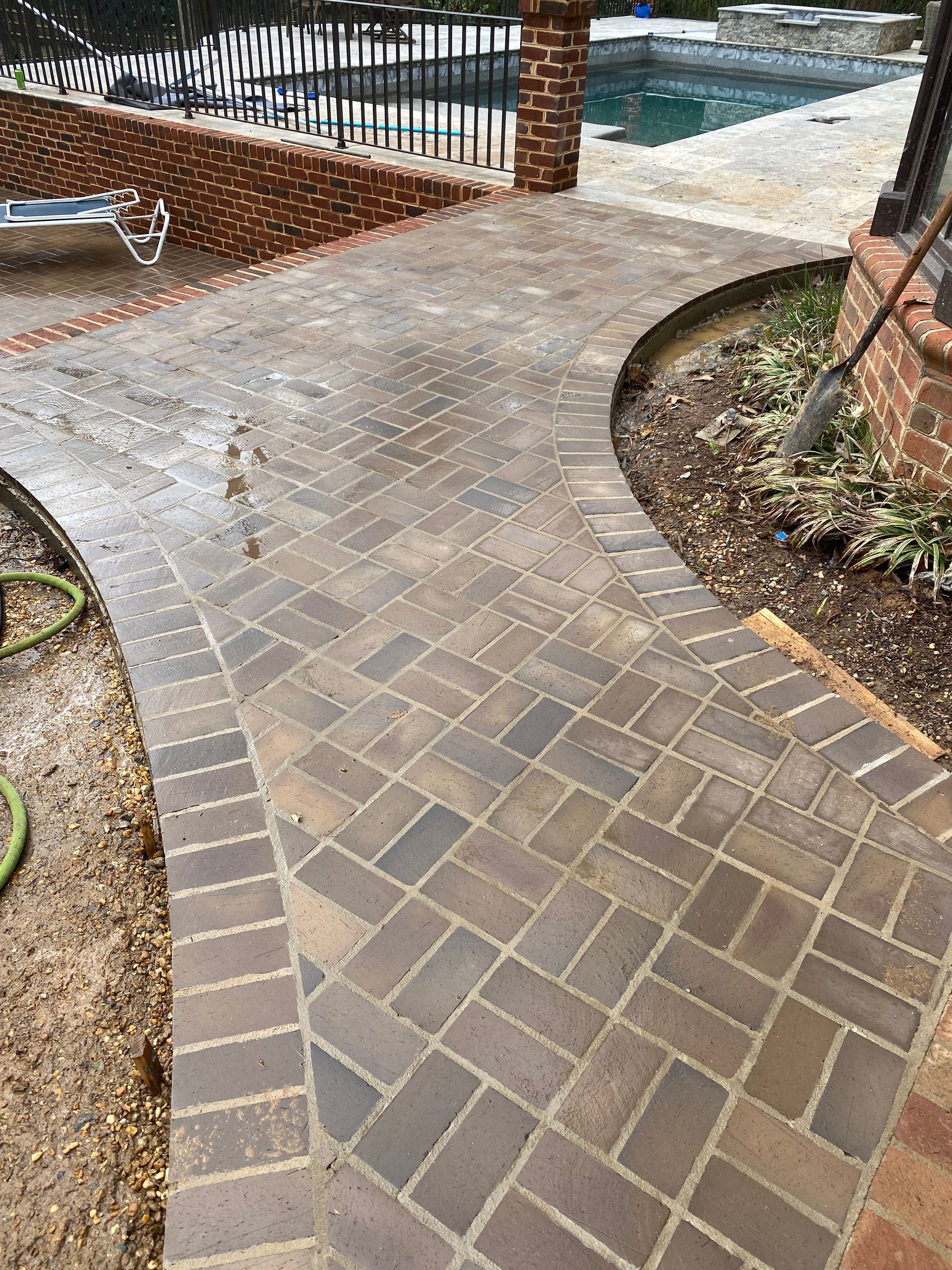 A brick walkway leading to a pool next to a brick wall.