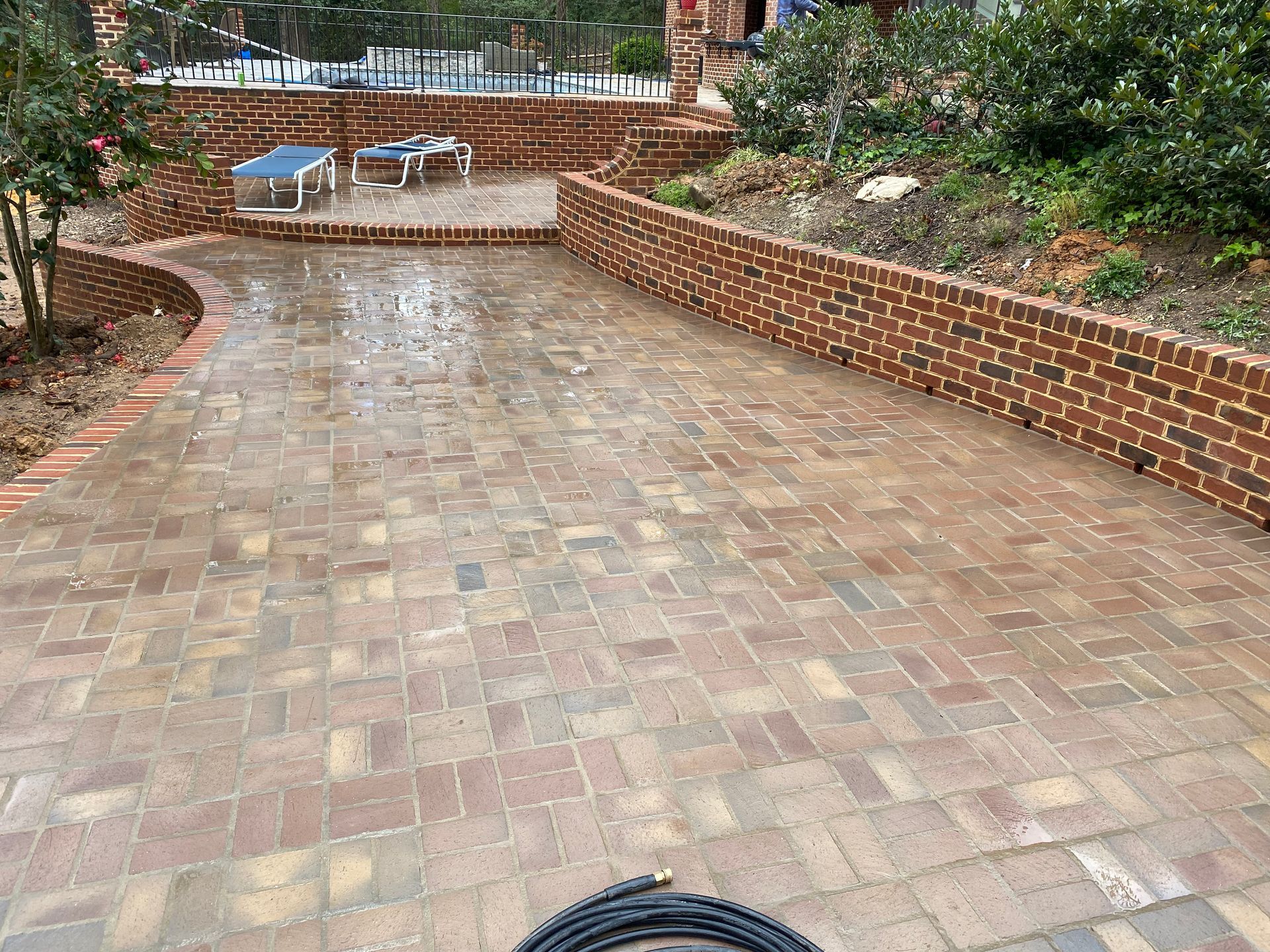 A brick patio with a pool in the background and a hose in the foreground.
