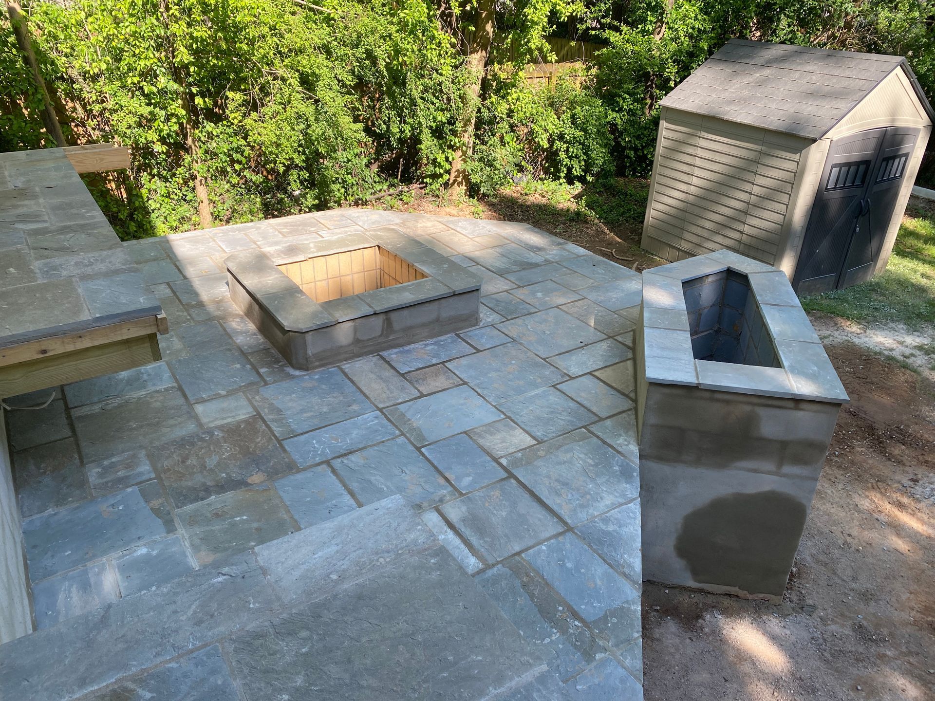 A fire pit is being built on a patio next to a shed.