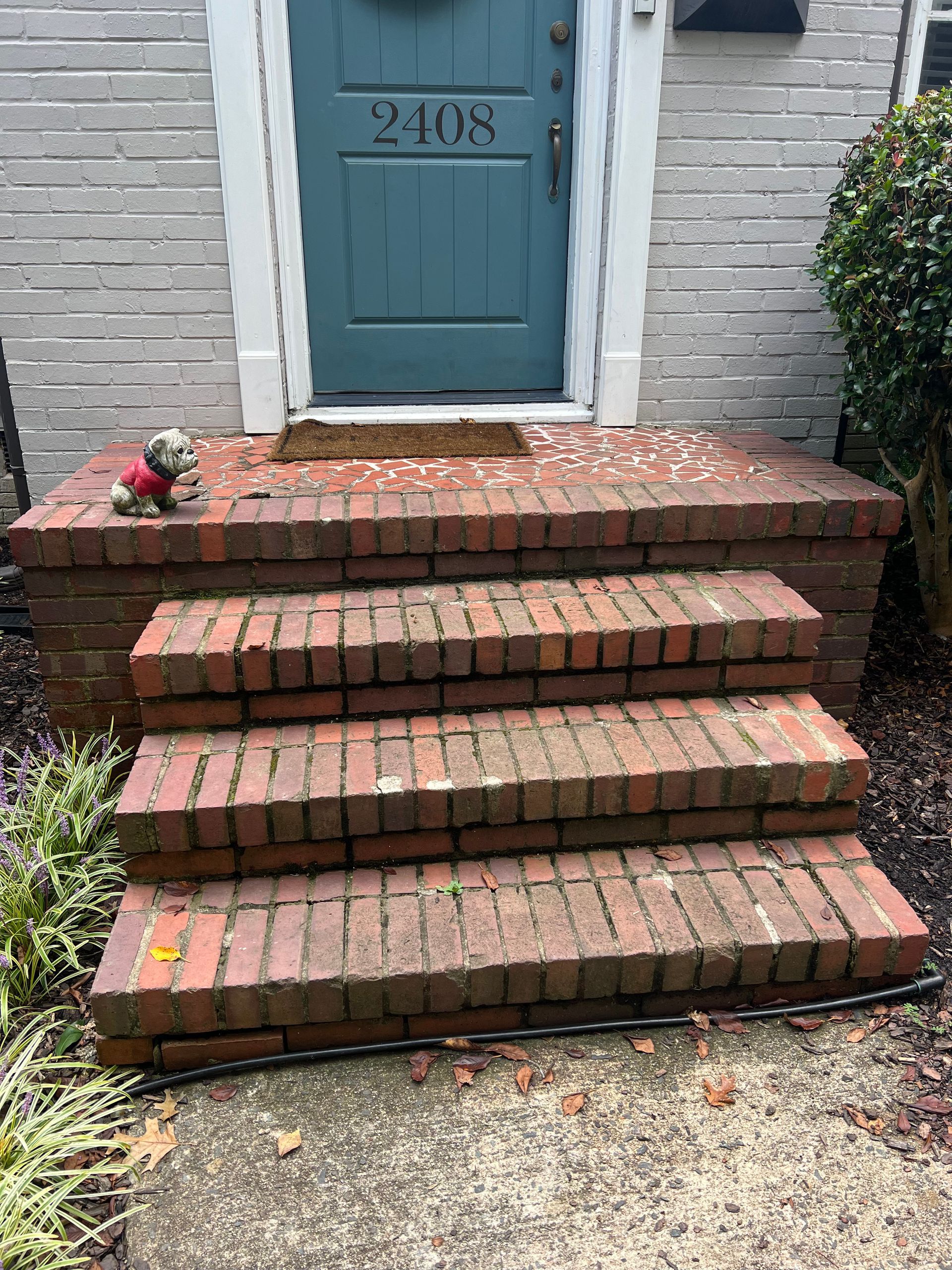 A teddy bear is sitting on a set of brick steps in front of a house.