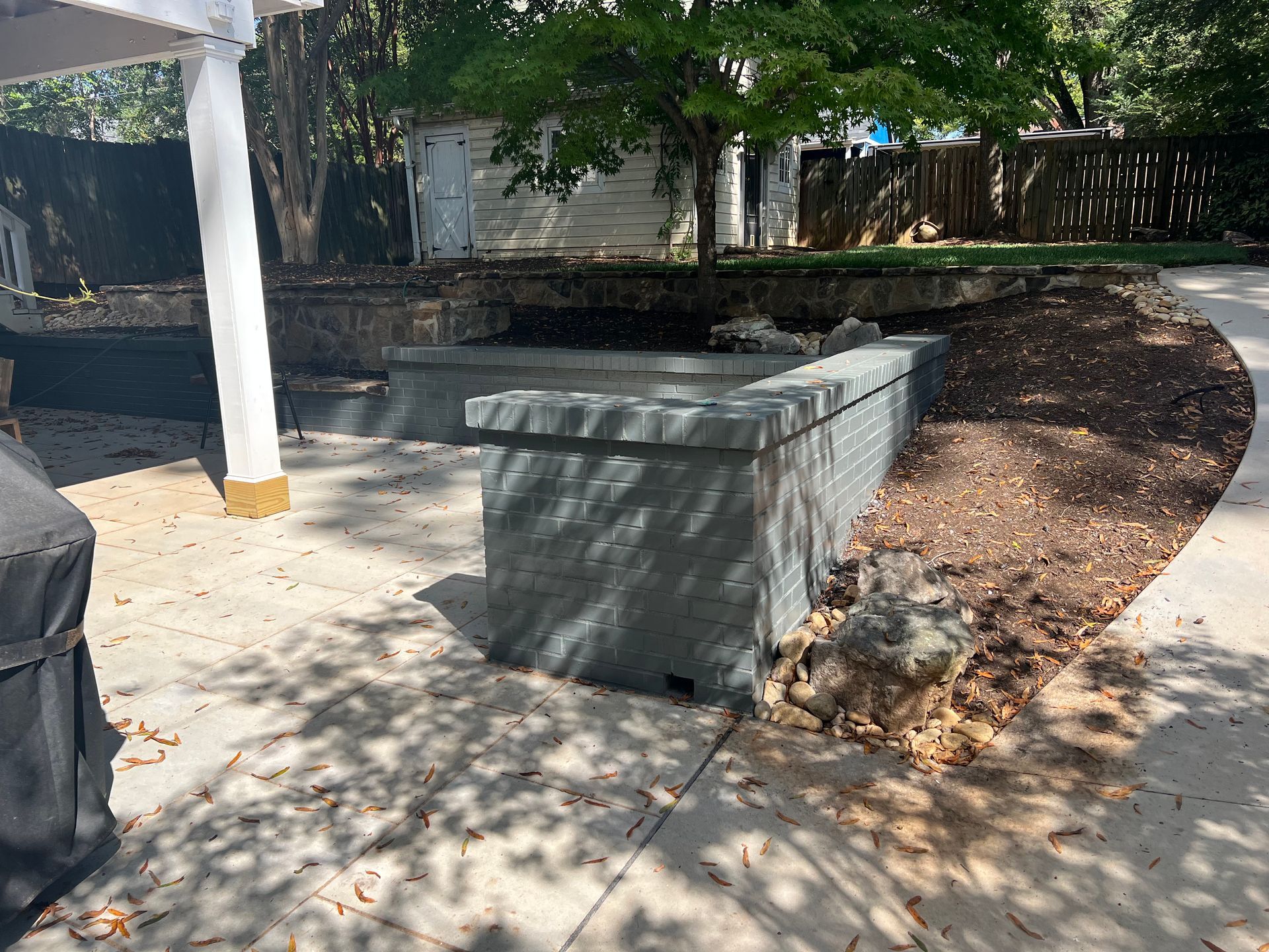 A concrete patio with a brick wall and a grill.
