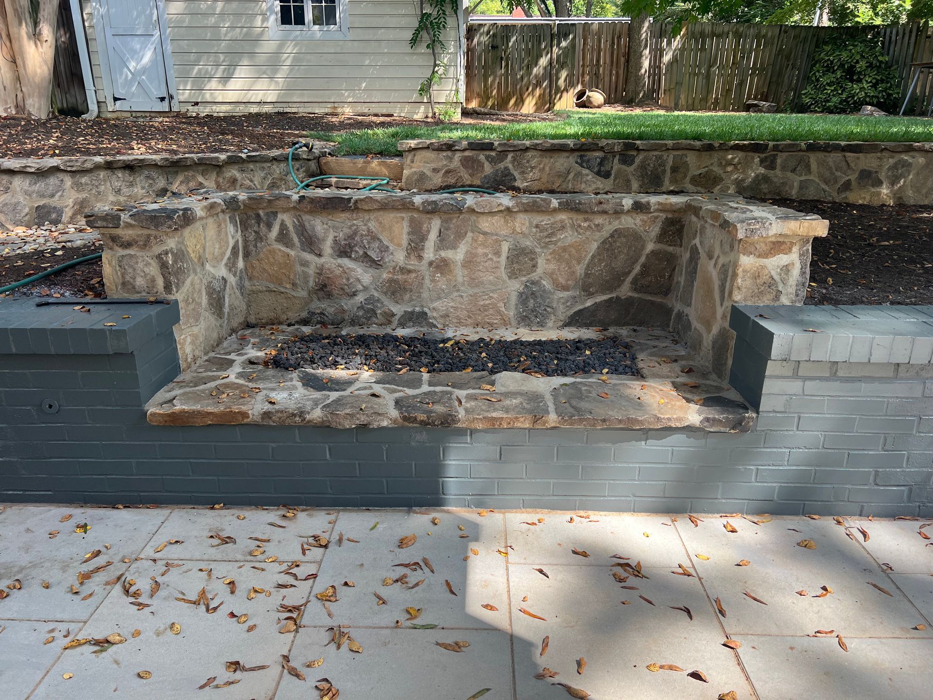A fire pit is built into a stone wall in a backyard.