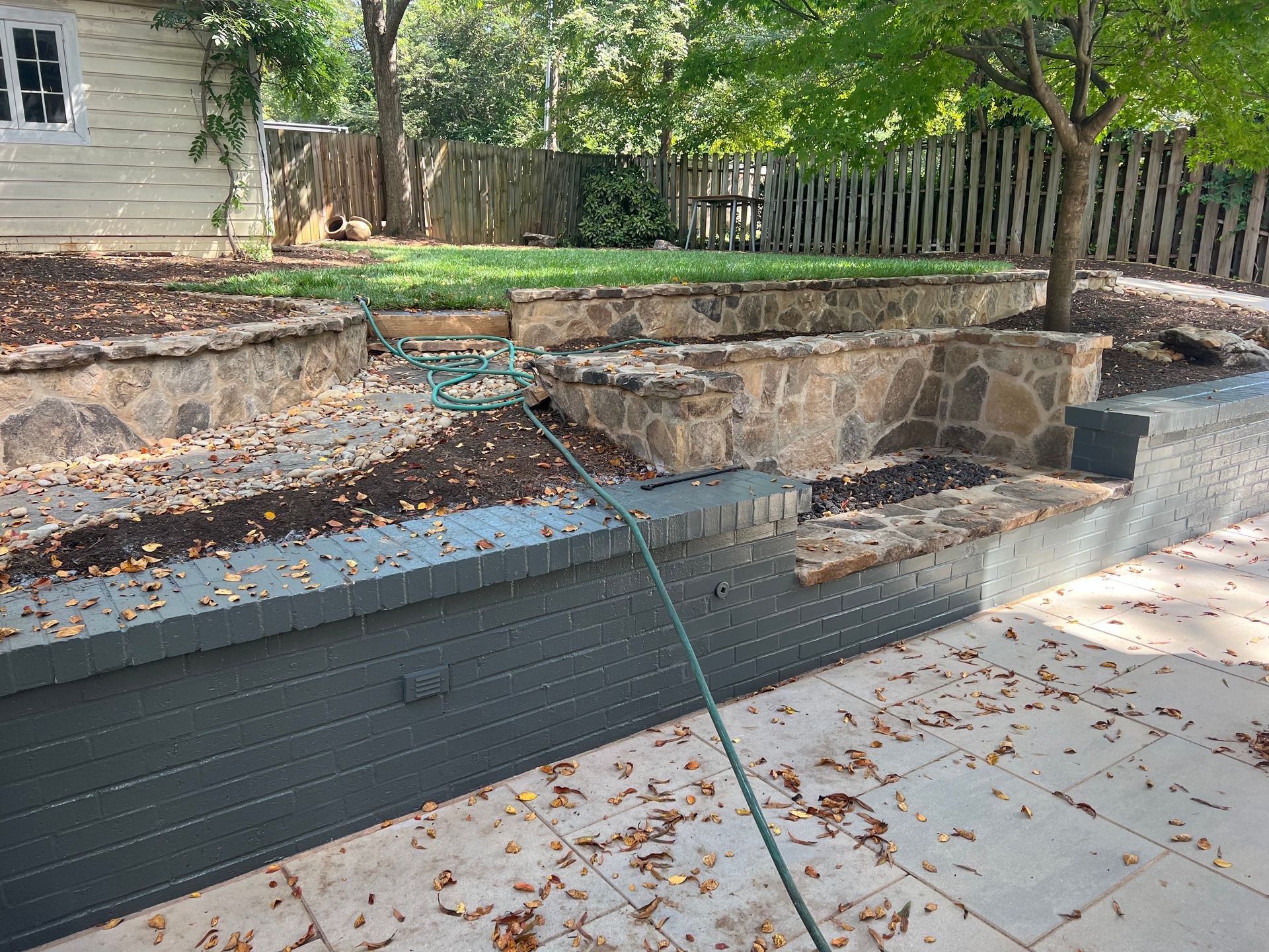 A person is spraying water on a patio with a hose.