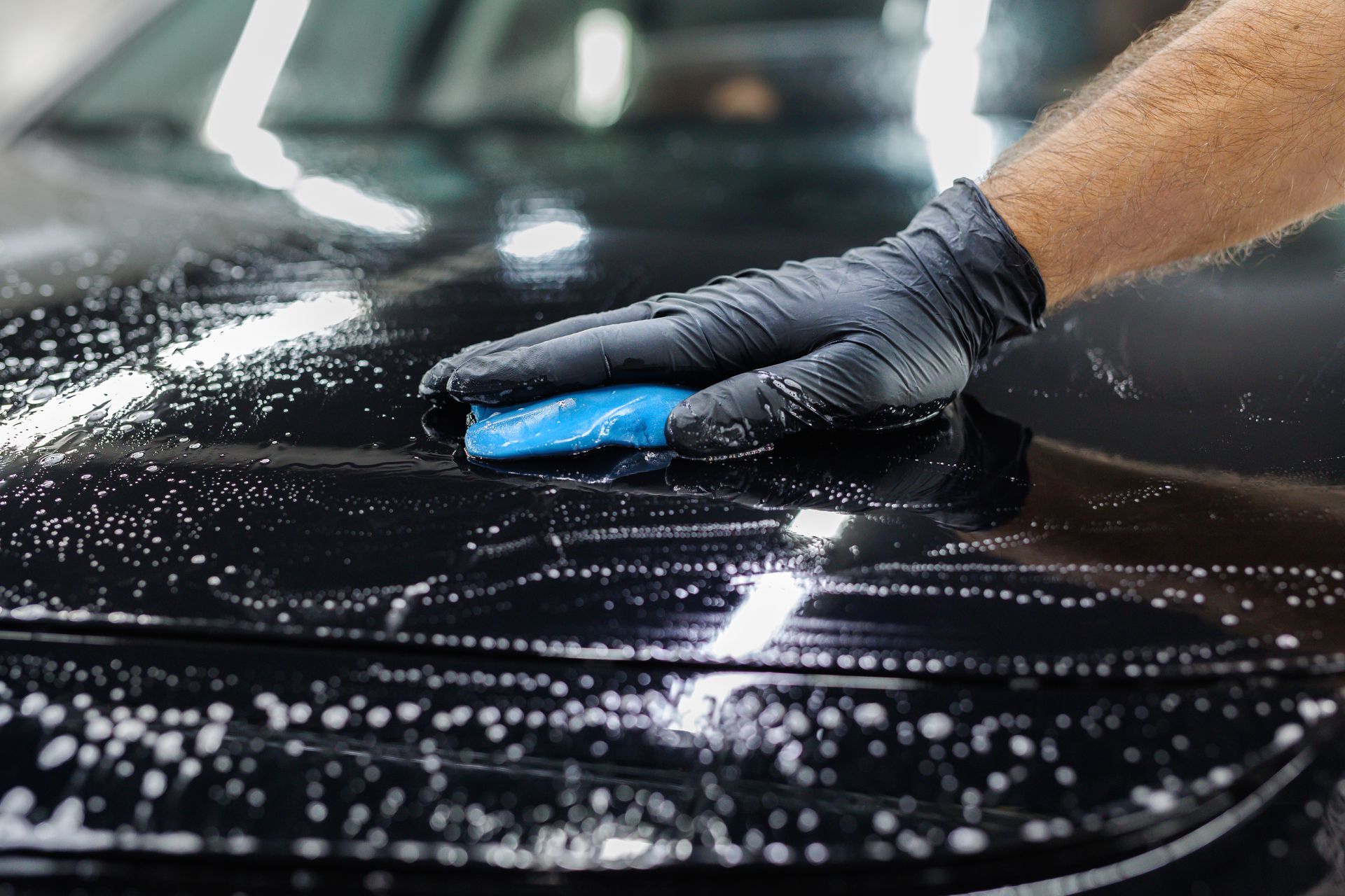 A person sprays black paint on a car's body panel in a paint booth.