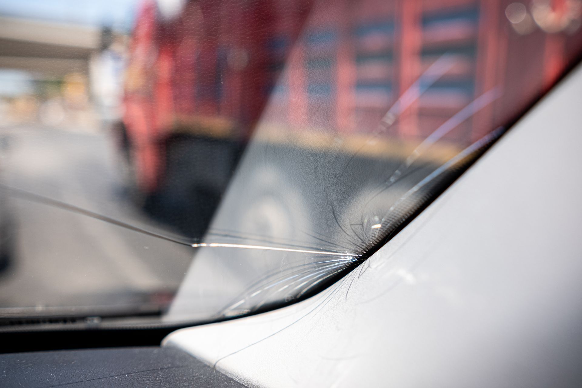 A long crack extending from the edge of a car windshield, with a blurred red truck visible in the background.