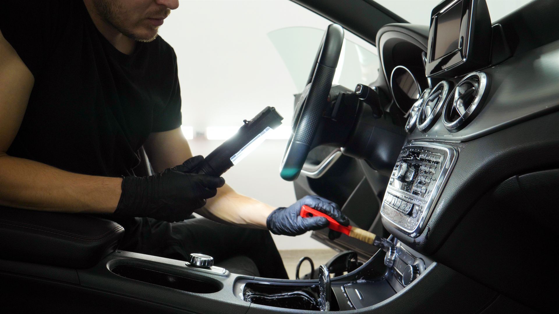 Person in blue glove cleaning a red car tire with a sponge.
