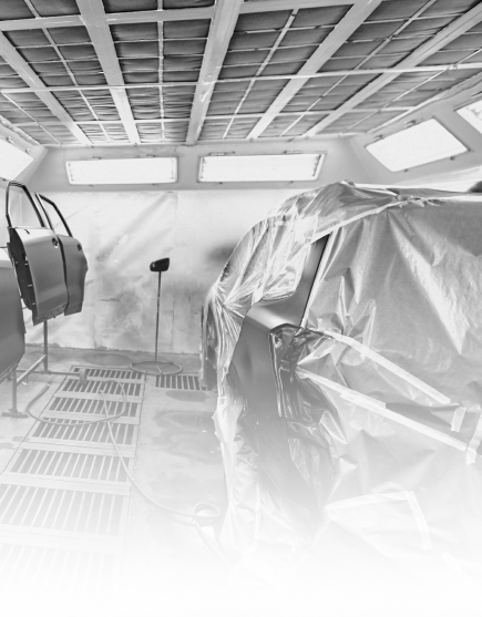 Black-and-white view of a workshop with a car covered in plastic and painting equipment nearby