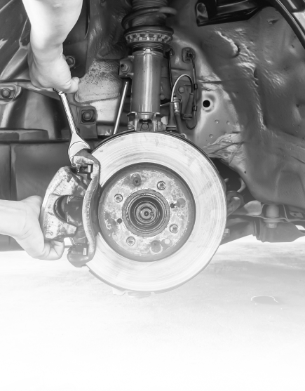Mechanic’s hands working on a car’s exposed brake rotor and suspension assembly | Total Auto Services