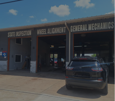 Auto repair shop with three service bays and a dark SUV parked outside under a blue sky.