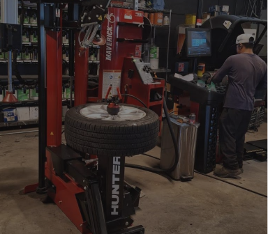 Auto shop tire-changing machine with a mounted tire and a mechanic working at a computer nearby | Total Auto Services