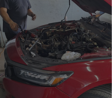 Red car with hood open, exposing the engine; person standing beside it in a garage. | Total Auto Services