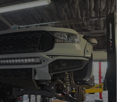Front of a white Ford truck on a lift in an auto repair garage, with exposed suspension parts. | Total Auto Services