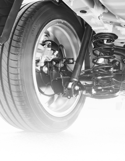 Close-up of a car’s rear wheel and suspension undercarriage in black and white.