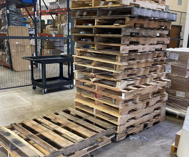 Pile of wooden pallets stacked in a warehouse, with another pallet on the floor.
