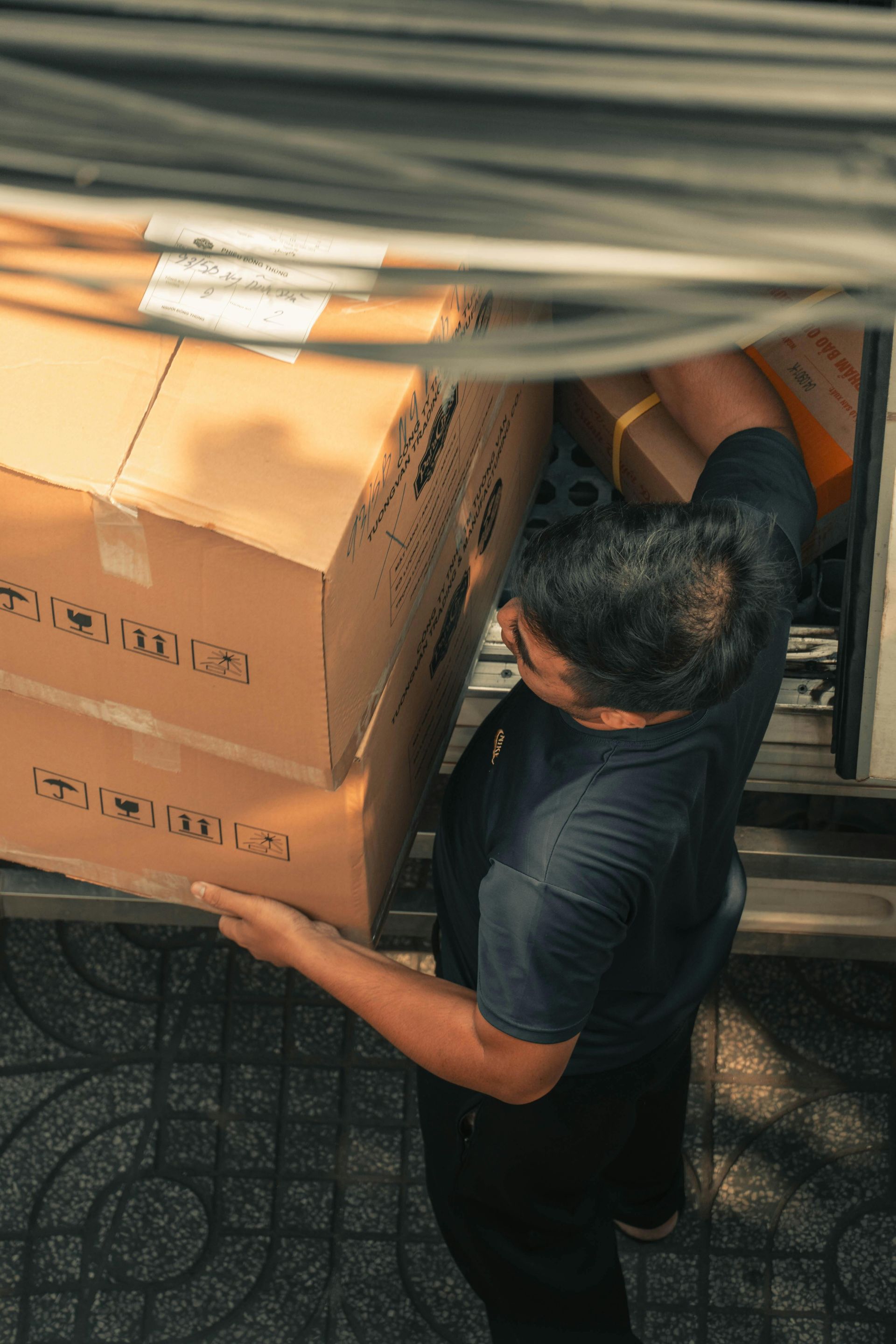 Person in black shirt loads cardboard boxes into a vehicle, seen from overhead.