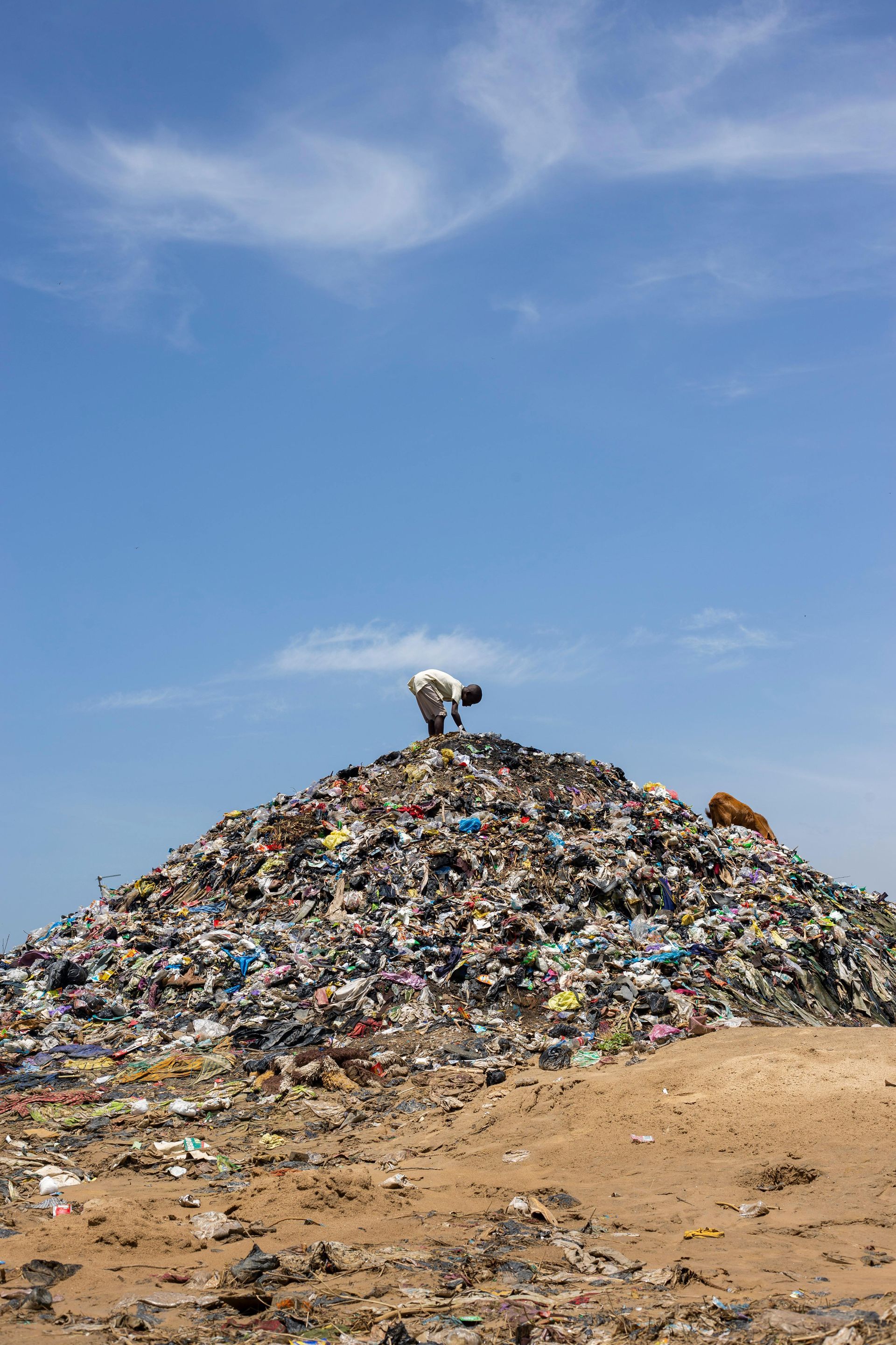 Man on large trash heap, blue sky background.