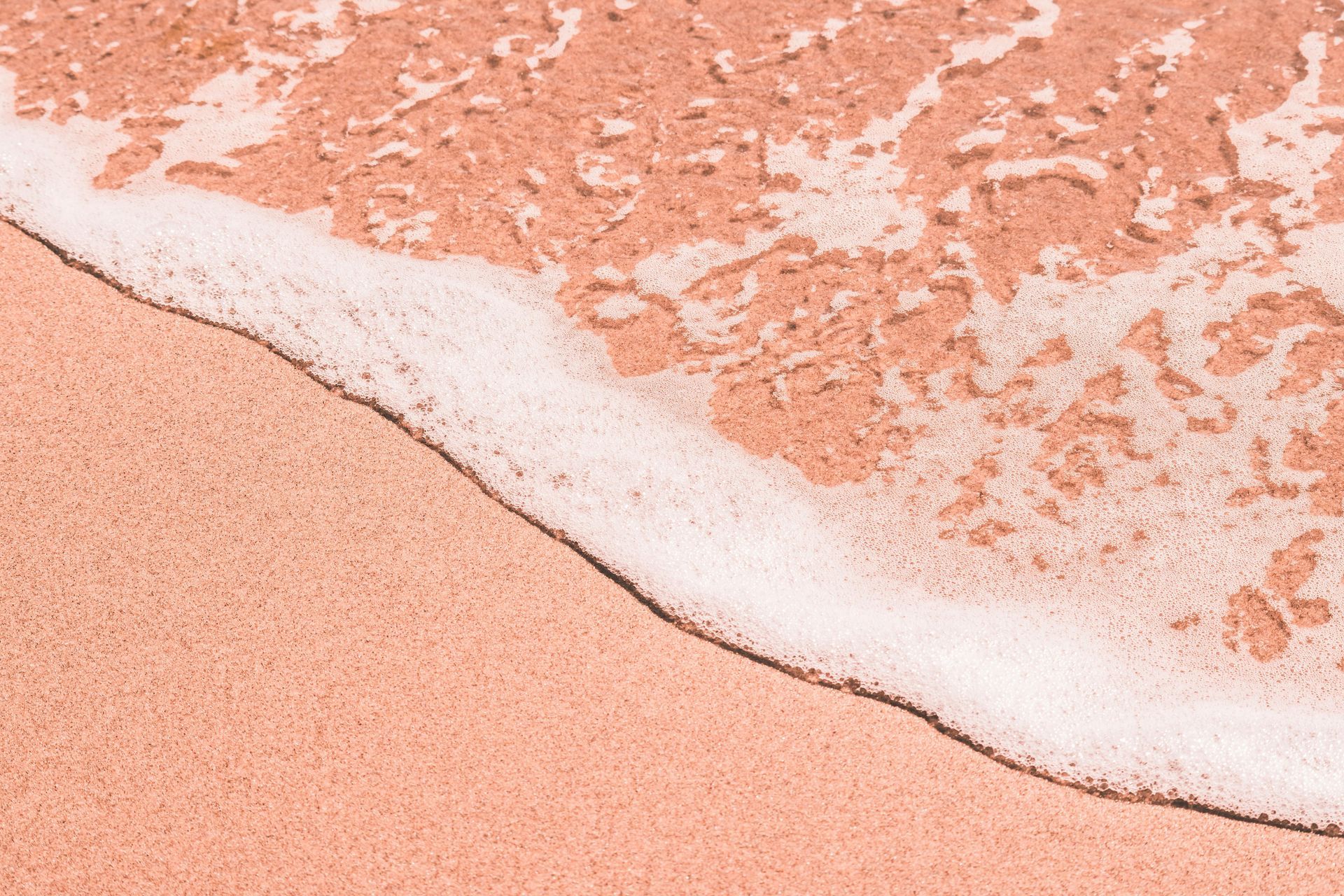 Pink sand beach with white foamy waves gently washing ashore.