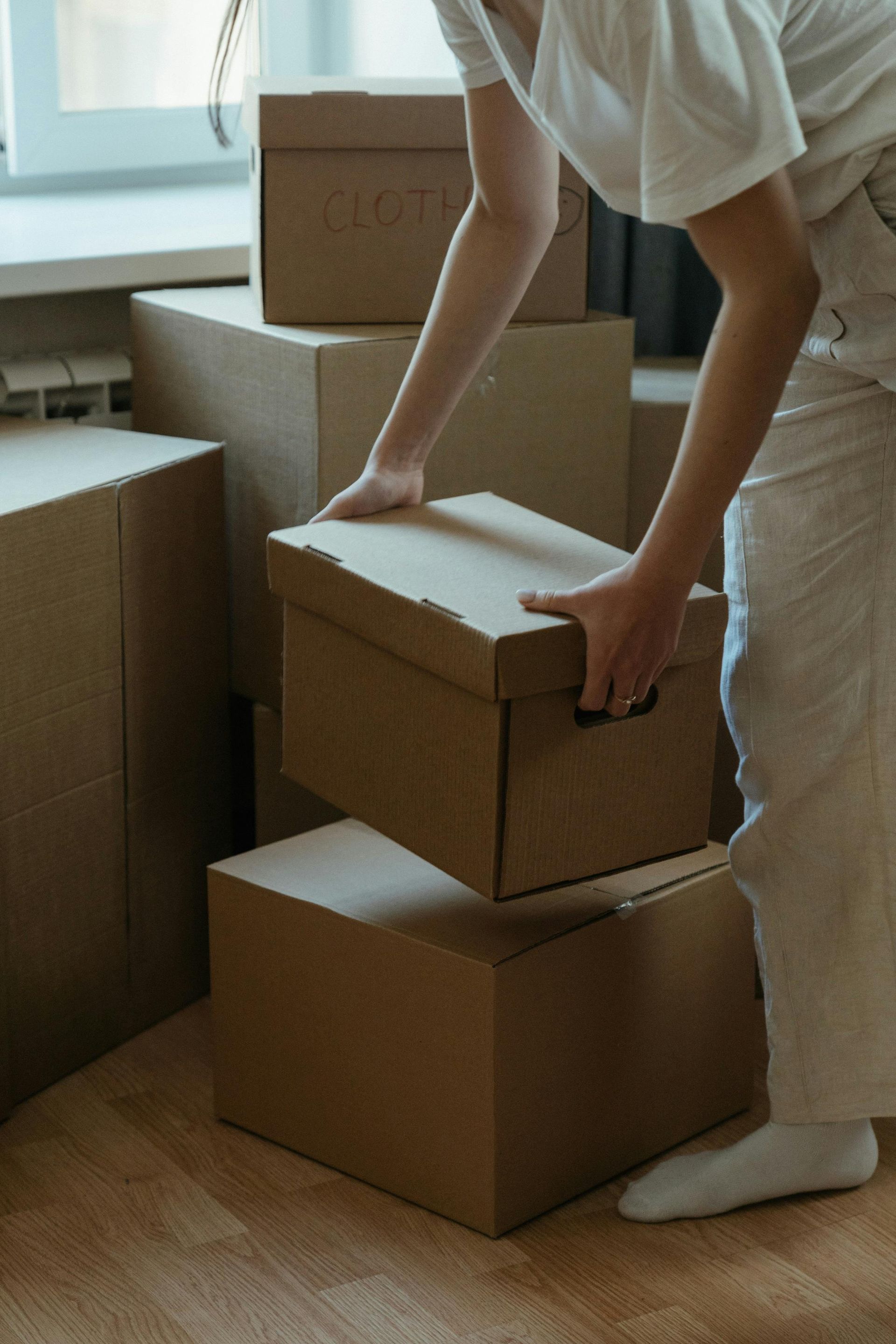 Person in white clothing lifting a cardboard box. Boxes stacked inside.