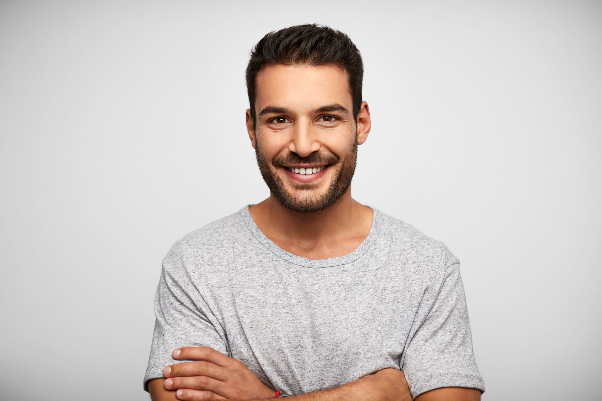 A man with a beard is smiling with his arms crossed.