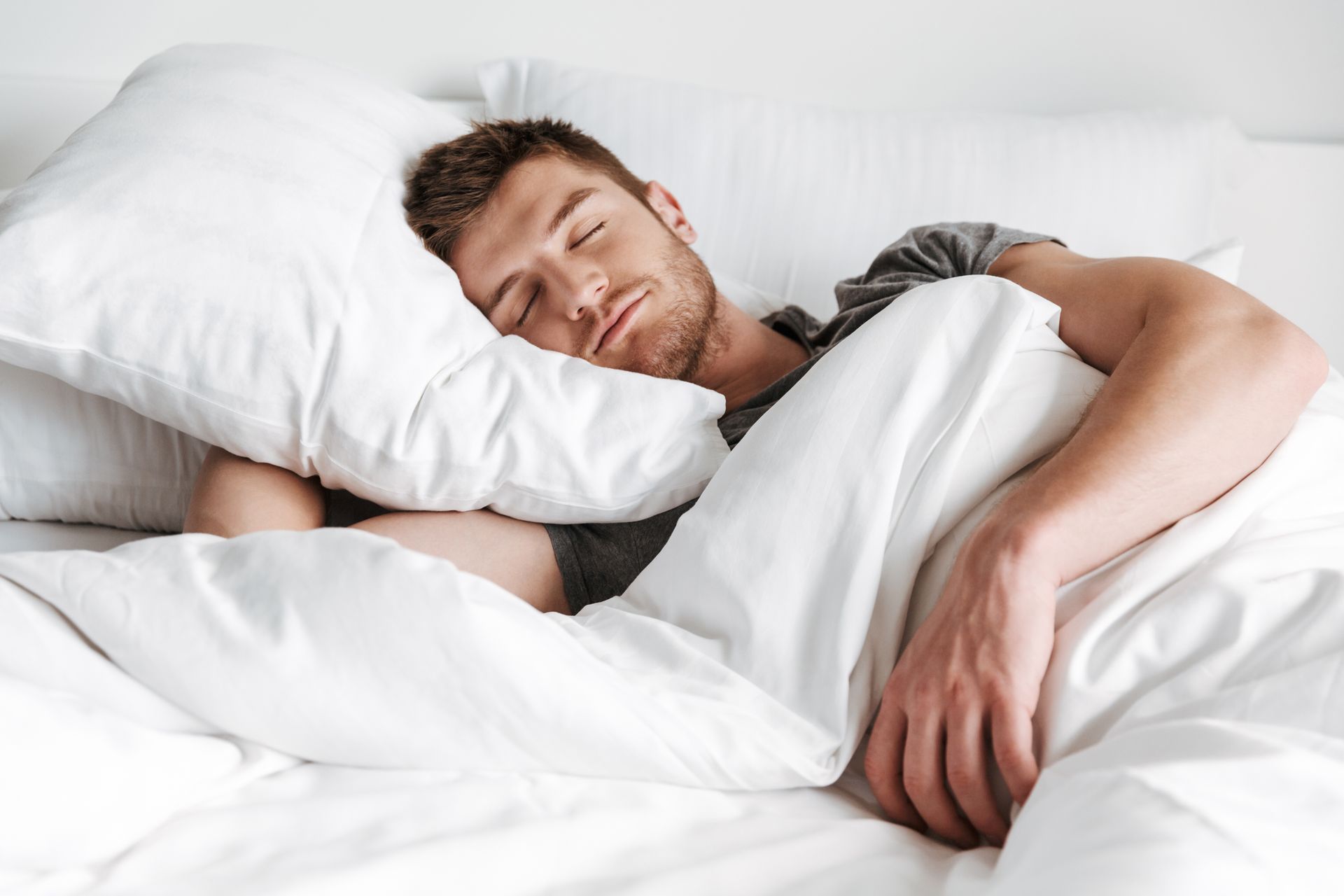 A man is sleeping in a bed with white sheets and pillows.