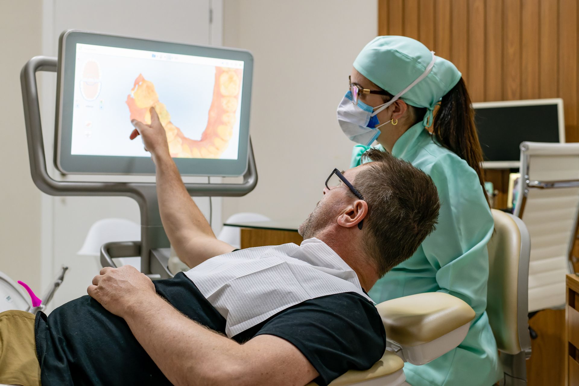 A man is sitting in a dental chair looking at a computer screen.