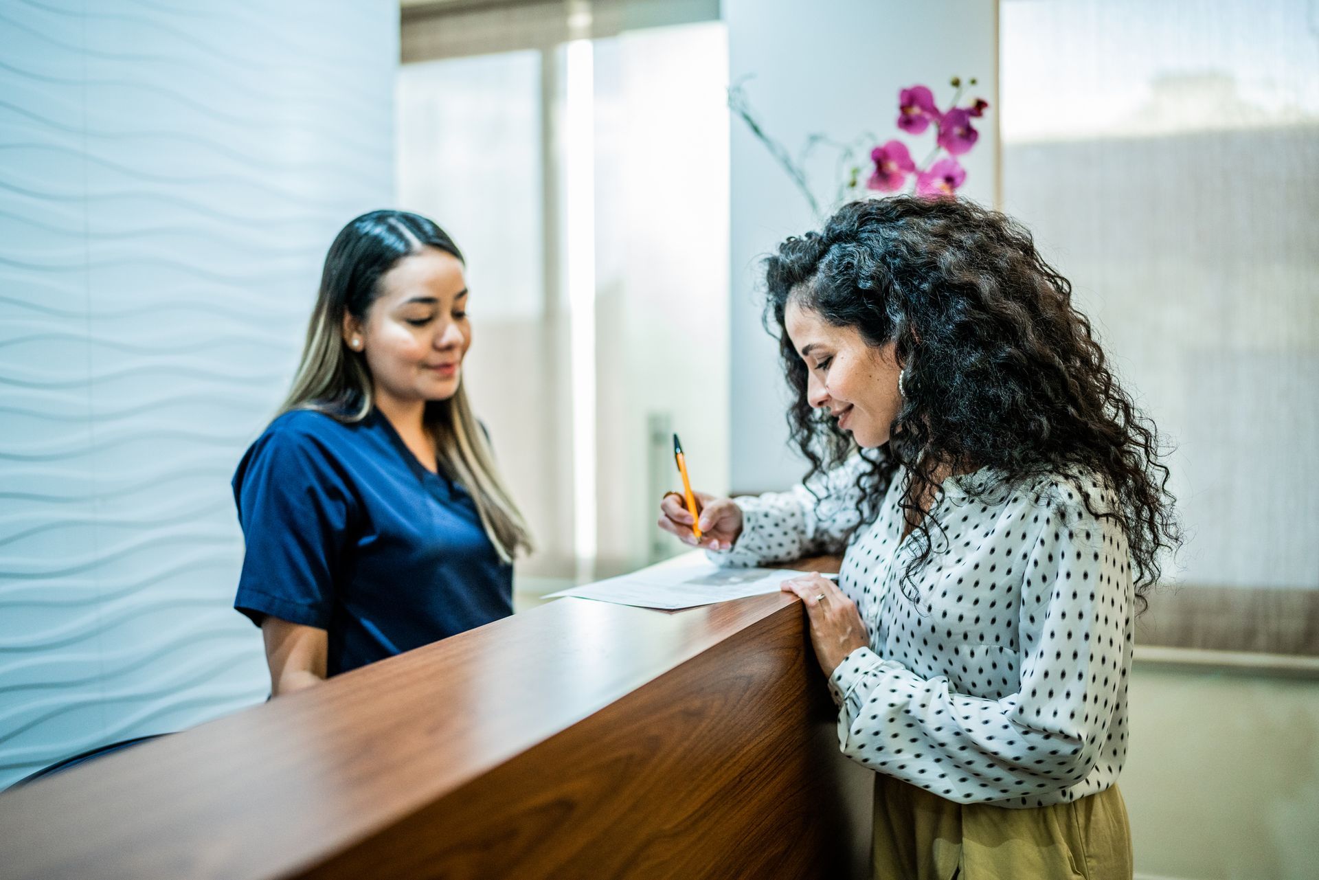 A woman is signing a form at a reception desk in a dental office.