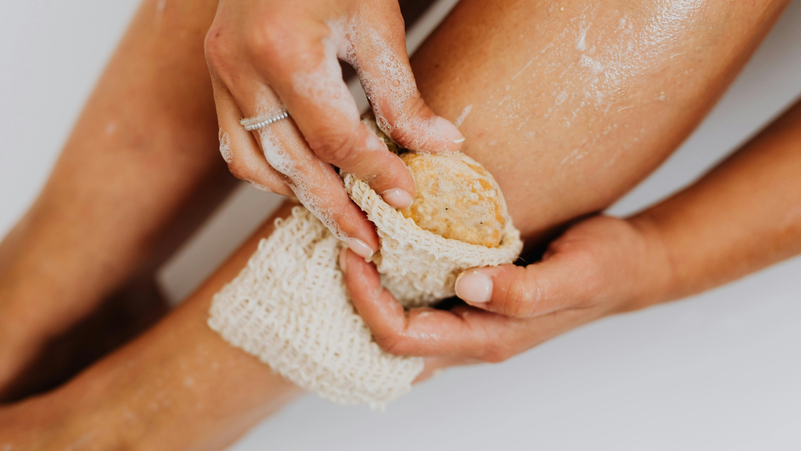 A woman is taking a bath and cleaning her legs with a sponge.