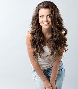 A woman with long curly hair is wearing a white tank top and blue jeans.