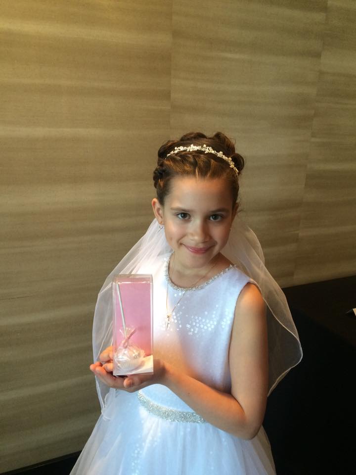 A little girl in a white dress is holding a pink box