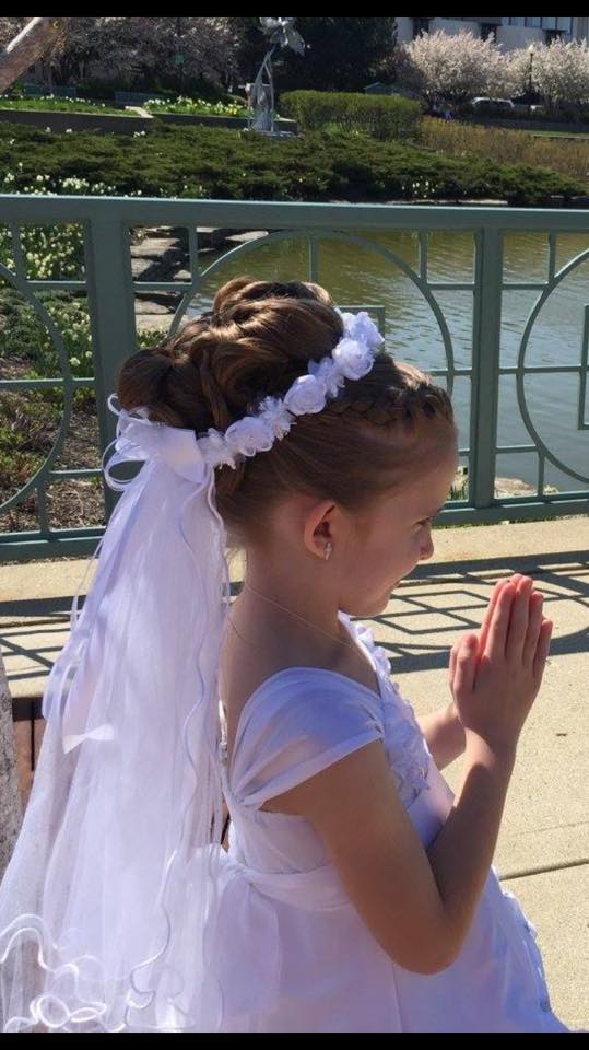 A little girl in a white dress and veil is praying.