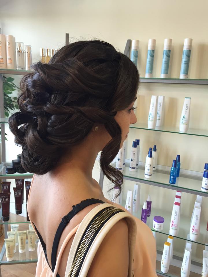 A woman with her hair in a bun is standing in front of a shelf of hair products.