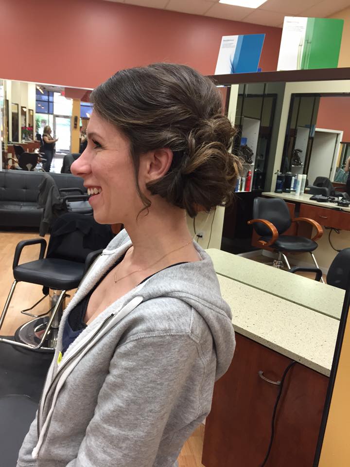 A woman is sitting in a chair in a salon with her hair in a bun.