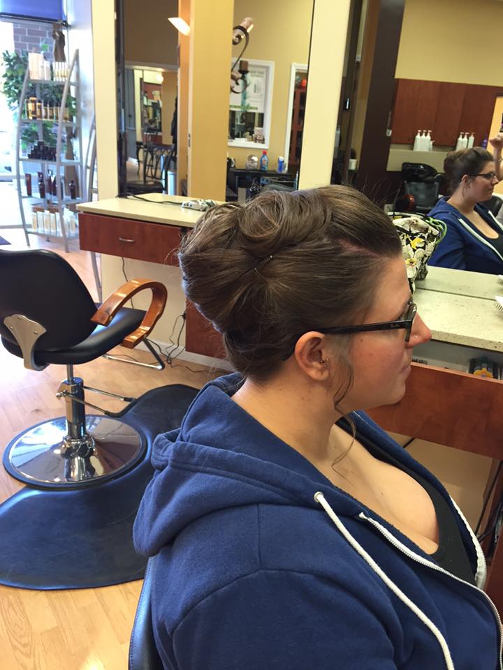A woman in a blue hoodie is sitting in a chair in a salon.