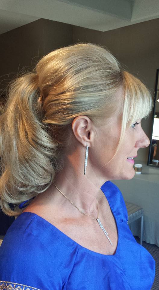 A woman in a blue shirt is wearing a ponytail and earrings.