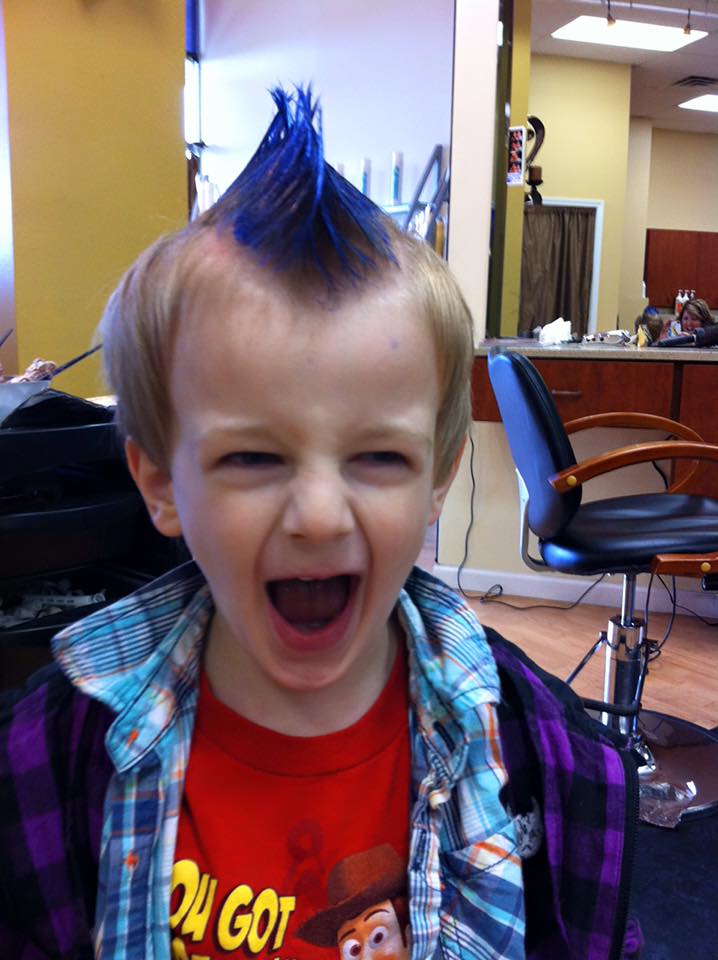 A young boy with a blue mohawk is wearing a toy story shirt