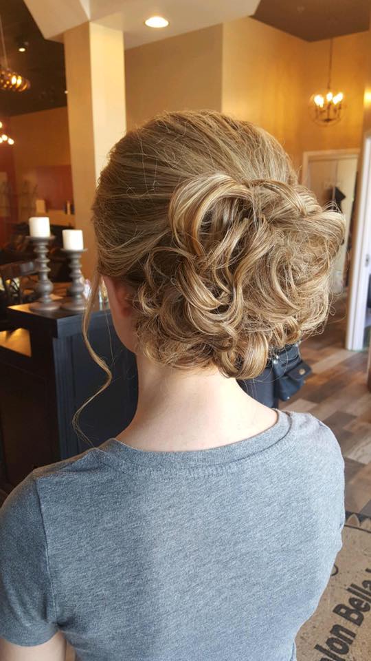 A woman is wearing a gray shirt and has her hair in a bun.