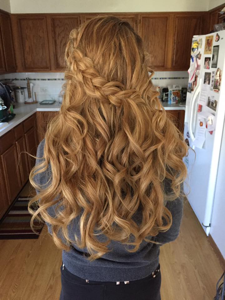 A woman with long curly hair is wearing a braided half up half down hairstyle in a kitchen.