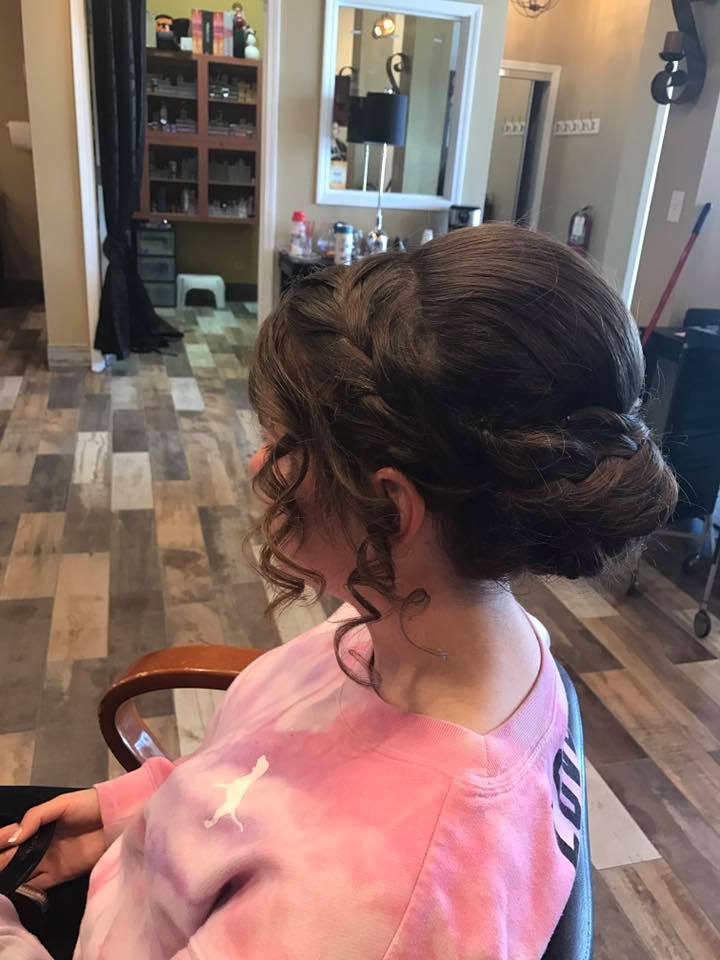 A woman is sitting in a chair in a salon with her hair in a bun.