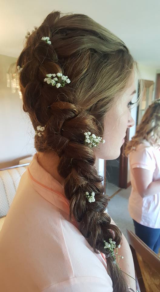 A woman is wearing a braided hairstyle with baby 's breath in her hair.