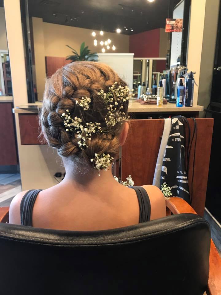 A woman is sitting in a chair with her hair in a braid and baby 's breath in her hair.