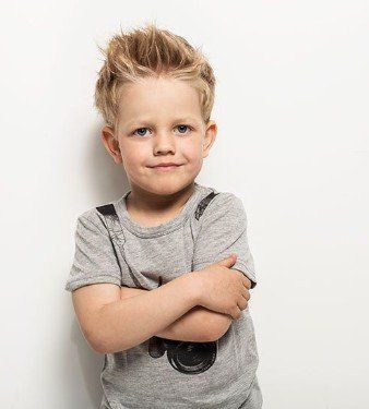 A young boy is standing with his arms crossed against a white wall.