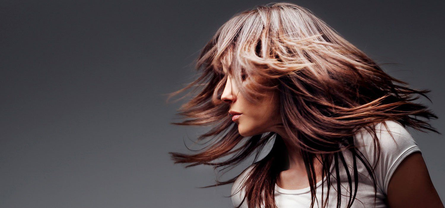 A woman with long brown hair is wearing a white shirt and her hair is blowing in the wind.