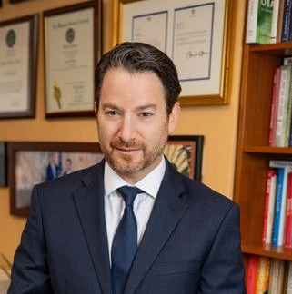 A man with a beard is smiling for the camera while wearing a blue shirt.