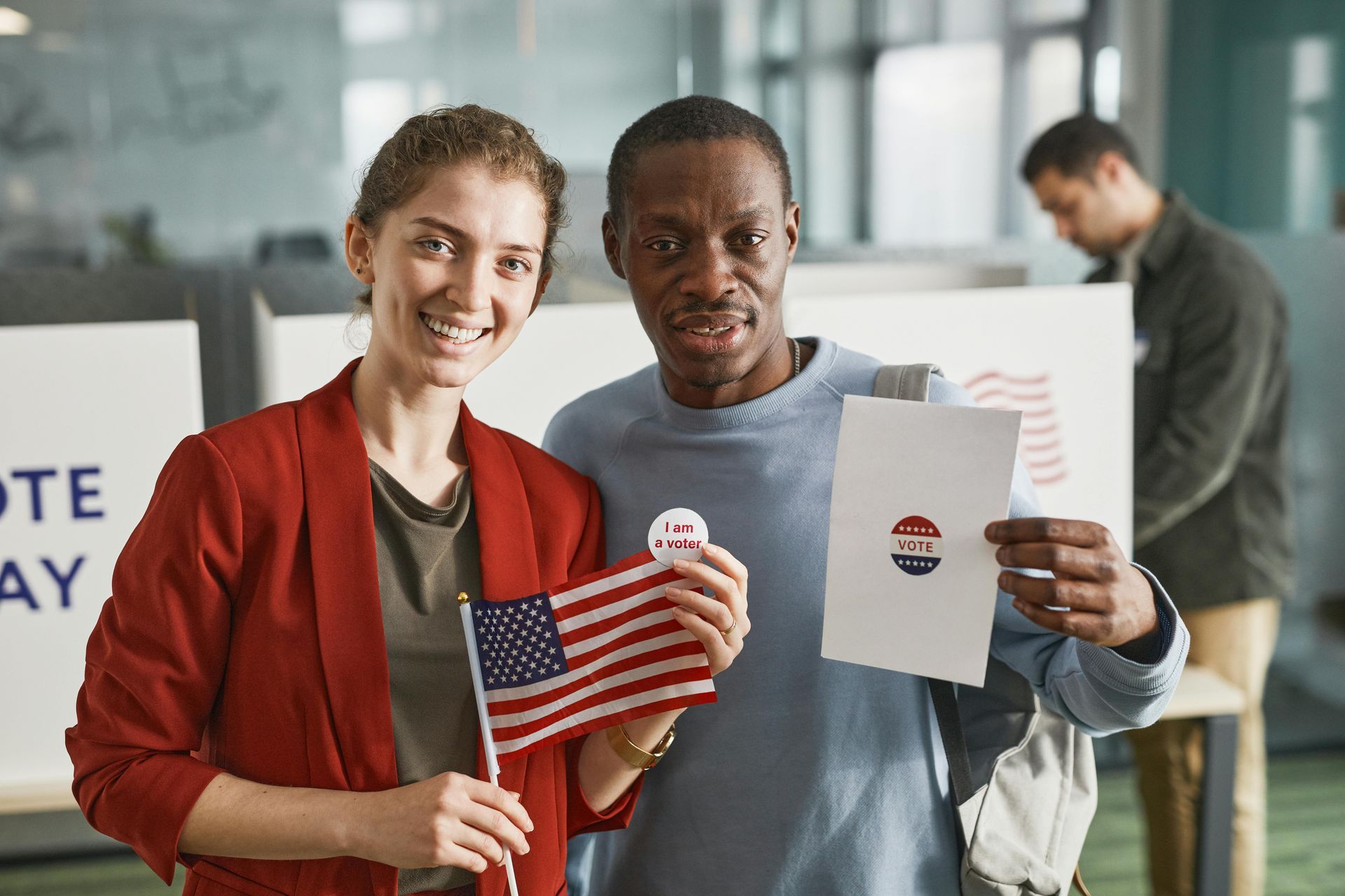 A man and a woman are holding american flags and a ballot.