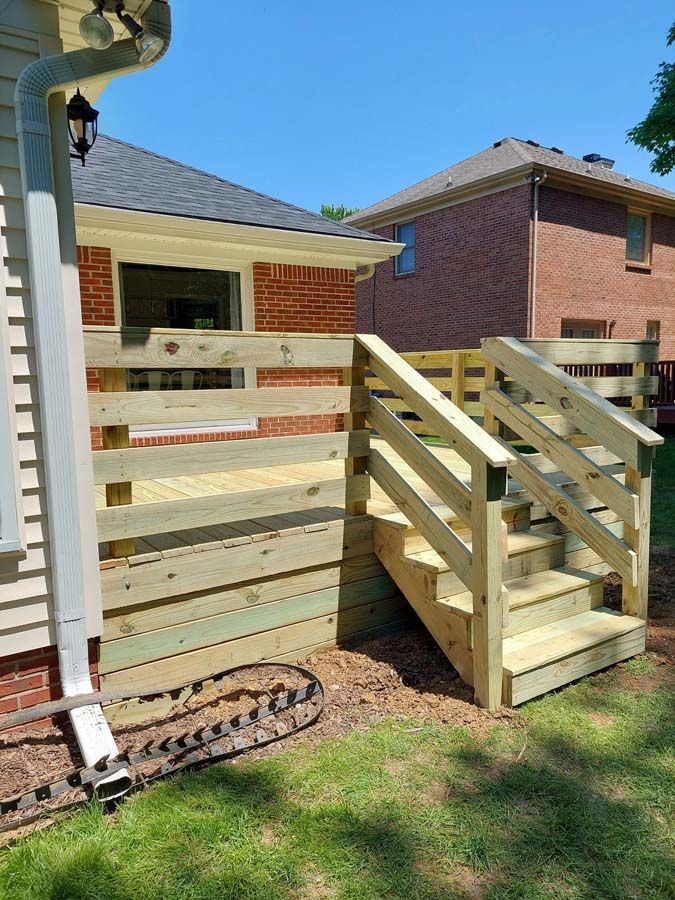 A wooden deck with stairs leading up to it is in front of a brick house.