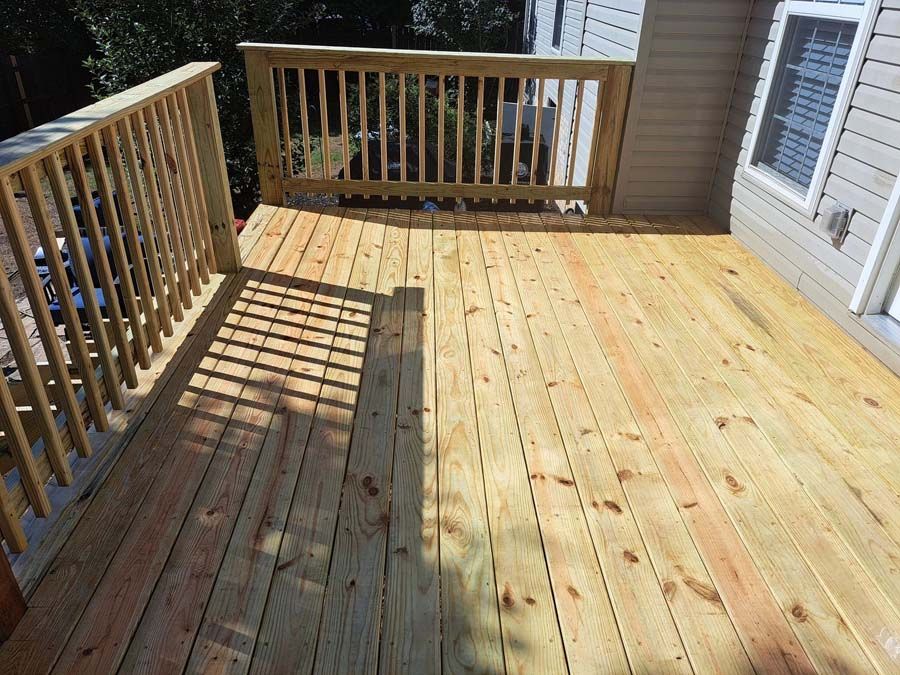 A wooden deck with a railing and a house in the background.