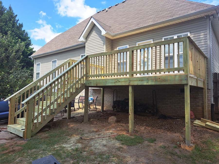 A wooden deck with stairs leading up to it is in front of a house.