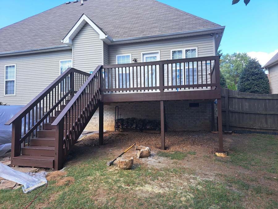 A wooden deck with stairs leading up to it is in the backyard of a house.