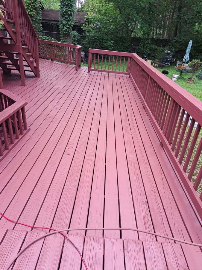 A red wooden deck with stairs and railing in a backyard.