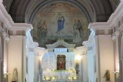 Altare della chiesa con arco decorato, statue e un affresco sovrastante, illuminato da candele soffuse.